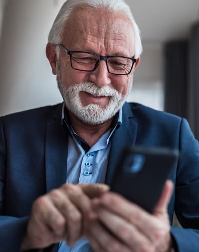 Person with glasses smiles and looks at a mobile phone.