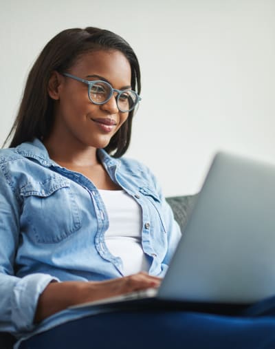 Person in glasses sitting on a couch with a laptop on their lap.