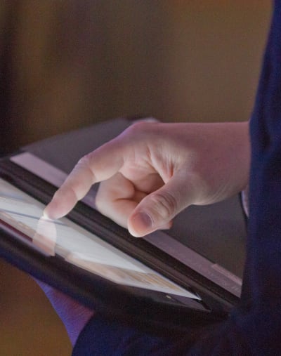 Close-up photo of a hand touching a tablet computer screen.