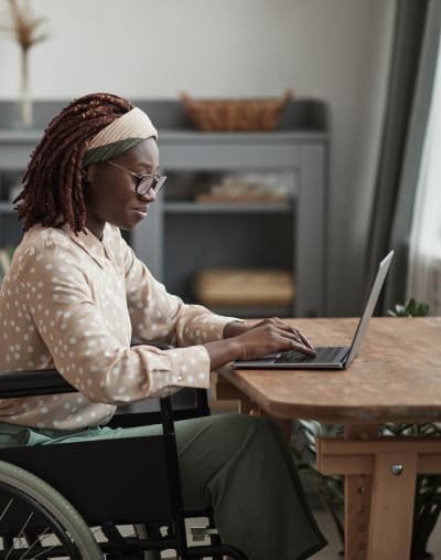 Person in wheelchair sits at a table in front of a laptop.