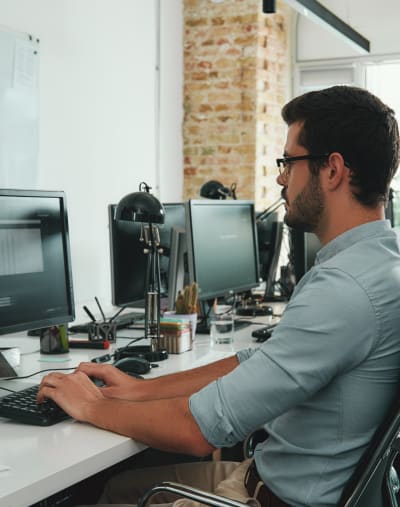 Person in business casual attire in an office environment typing on a computer keyboard.