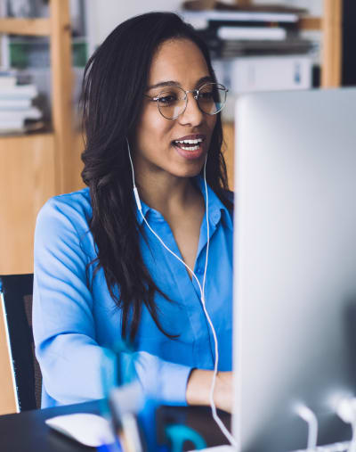 Person with glasses and headphones sits and looks at a computer monitor.