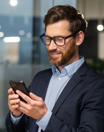 Person with glasses smiles and looks at a mobile phone.