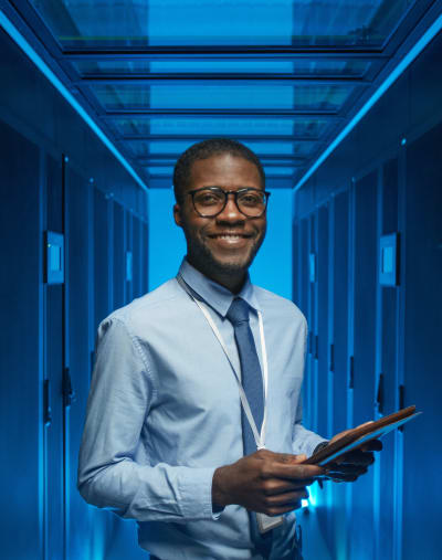 Person wearing a tie and glasses smiles and holds a tablet.