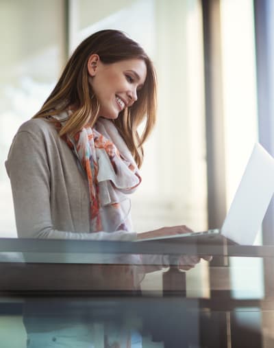 Person stands, smiles and looks at a laptop in an office.