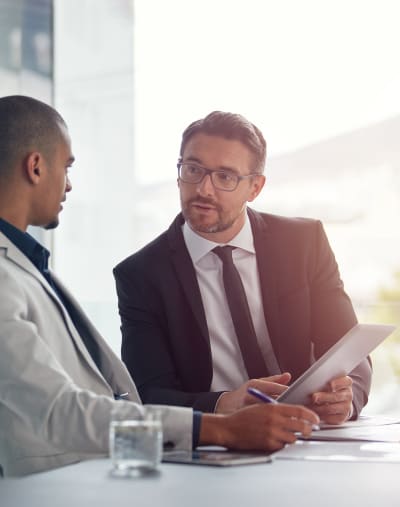 Two people sit in an open office and look over a contract on a tablet.