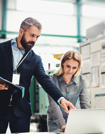 Two professionals review logistics strategies on a laptop in an open office setting.