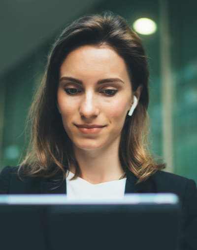 An employee with earbuds works on their laptop in an office building.