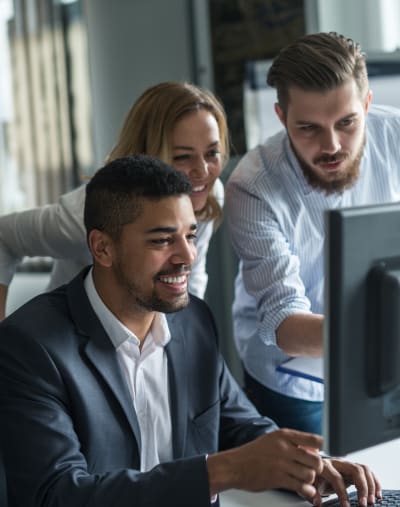 Three coworkers collaborate around a desktop computer as they discuss solution upgrade options.