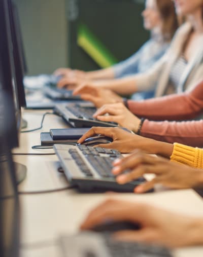 Close-up of hands working on desktop keyboards down a long table.