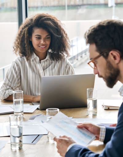 A consultant sits with a laptop at a table alongside a customer to provide training.