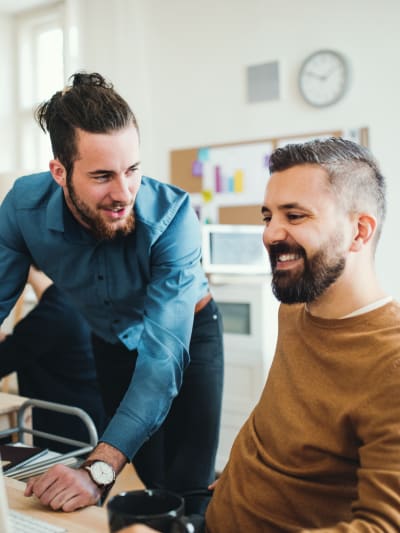 Two people smiling at a monitor while discussing