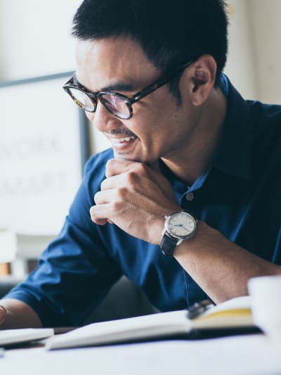 A young business person sits in an office with a laptop and a lush green plant.