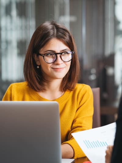 Two people in an office setting sit at a desk, reviewing metrics in a bar graph.