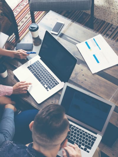 Aerial photo of three people sitting at a wood desk with two laptops open.