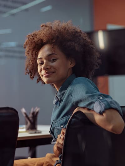 Person sits in conference room, turned around in seat and smiles at camera.