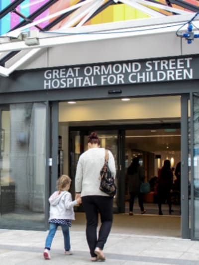 An adult and child walk hand in hand inside Great Ormond Street Hospital for Children.