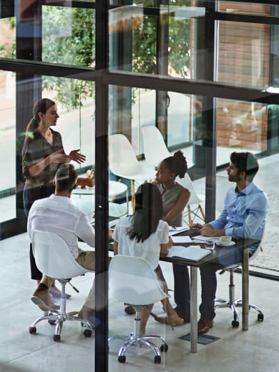 People sit in a conference room with glass walls and windows in an office.