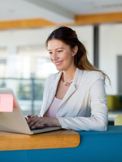 Person in white jacket uses a laptop in a modern office setting.