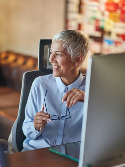 Person in blue button-down shirt sits at a desk in front of a desktop computer.