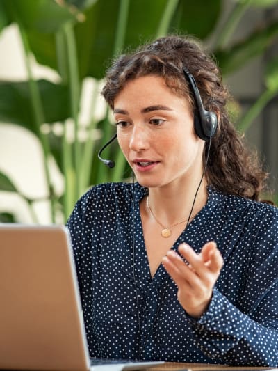 Person wearing a headset talks to someone through their laptop.