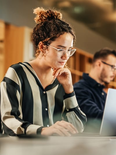 Person in striped blouse sits at a desk and works on a laptop.