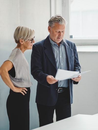 Two people stand in an office and look at paperwork.