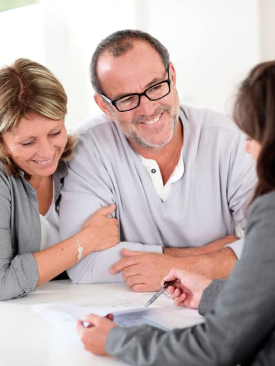 Two people smile and embrace as they look over paperwork with a credit union employee.