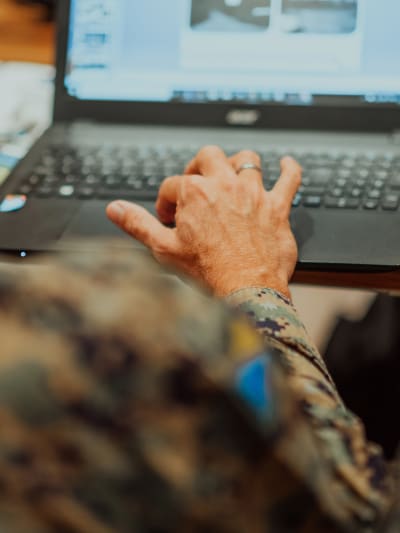 Person wearing military fatigues uses laptop computer. 