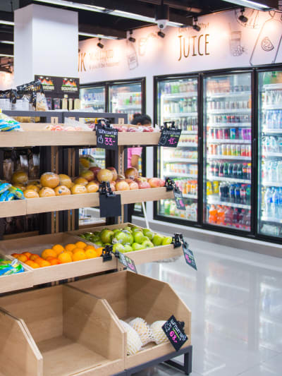 The interior of a convenient store with fresh produce as well as a wall of cold beverages.