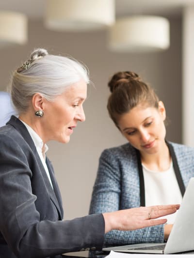 Two people sit at a table, talk and look over information on a laptop.