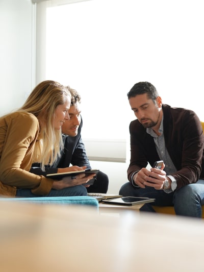 Three people sit and look closely at information on a mobile phone.