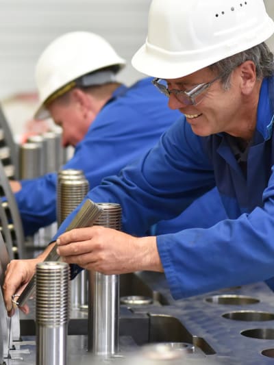 Two industrial workers in hard hats work on turbines.