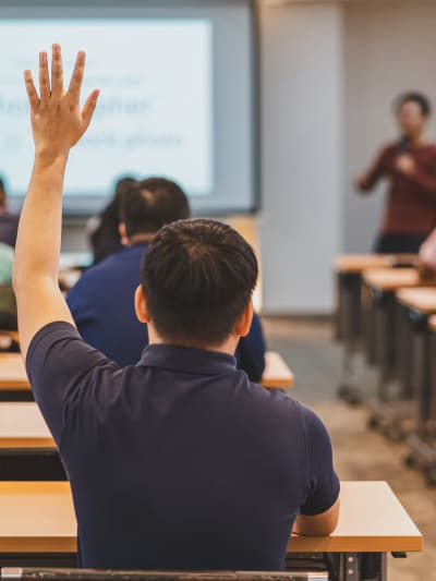 An engaged college or university student raises their hand to ask their professor a question in class.