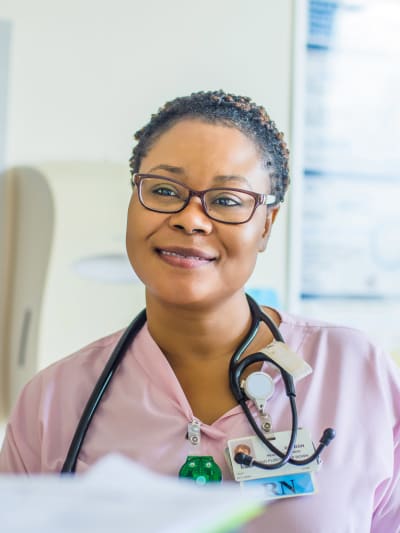 Medical professional wearing pink scrubs and a stethoscope smiles in a healthcare setting.