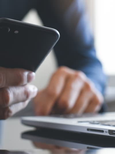 Person holds a cell phone while sitting in front of a laptop and calculator.