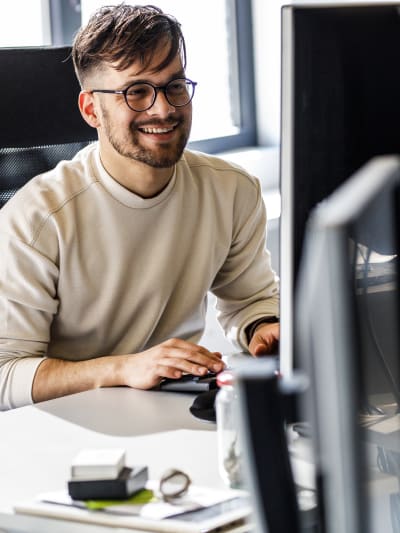 Person with short dark hair and glasses uses a desktop computer in an office.