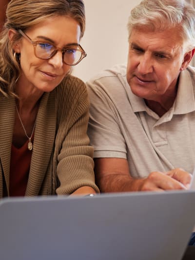 Two people reference a laptop screen while one holds a stack of white papers.