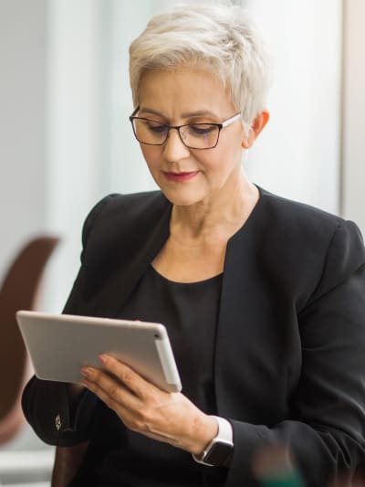 Person in dark suit sits in a wooden chair, working on a tablet computer.