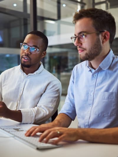 Two young professionals collaborate at a desktop computer.