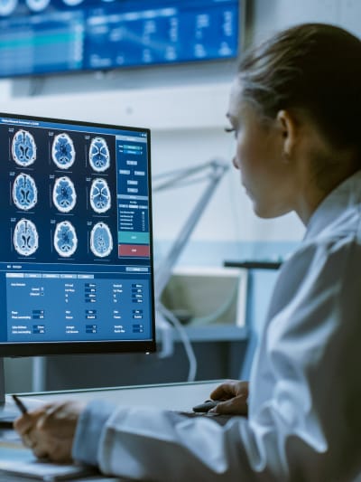 A woman in a doctor's coat looking at brain image scans.
