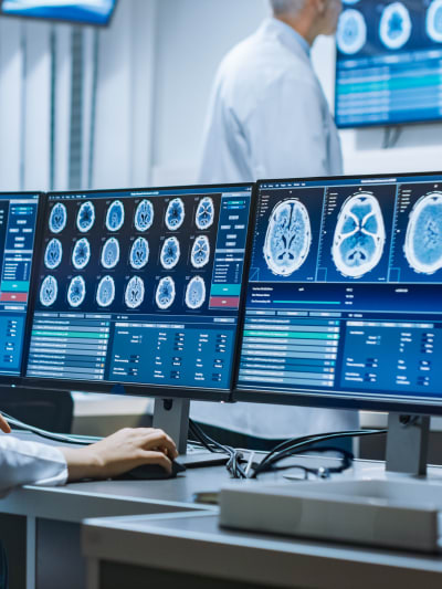 Woman neuroscientist surrounded by monitors showing brain scans