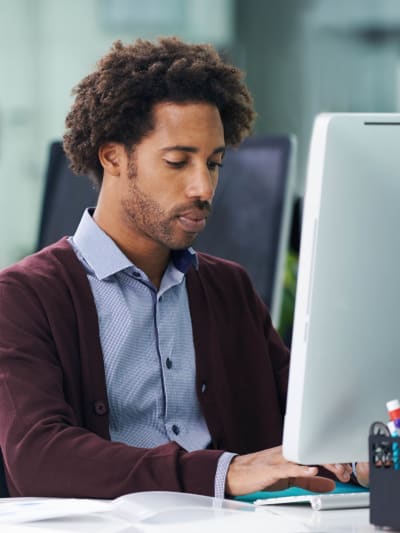 Person in plum sweater works at a desktop computer.