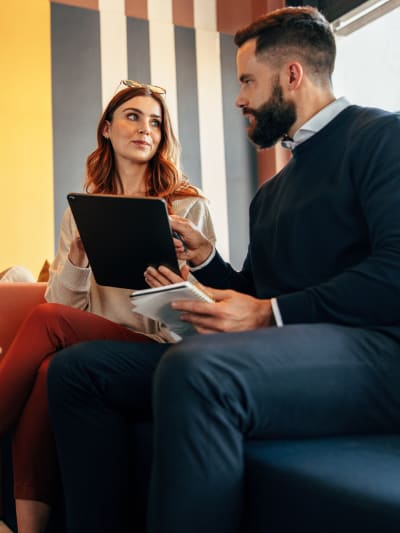 Two coworkers sitting on a couch, looking at a laptop