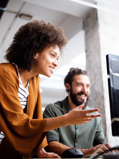 Two coworkers collaborate on a desktop computer. 