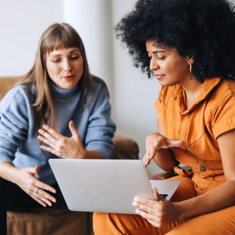 2 girls discussing and one of them holding a laptop 