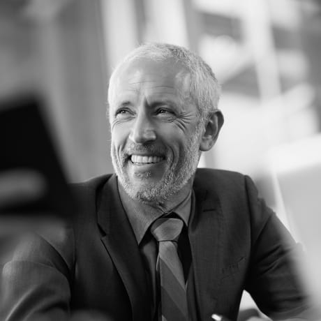 Black and white photo of a person in a dark suit, smiling.