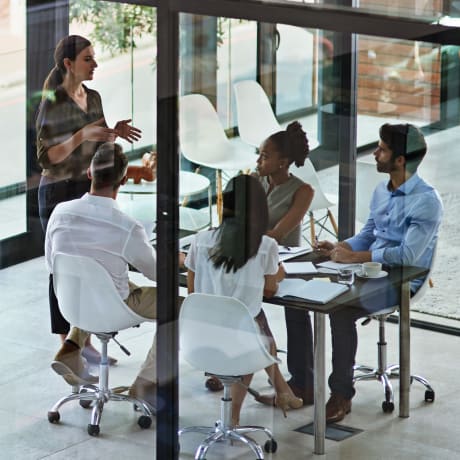 People sit in a conference room with glass walls and windows in an office.