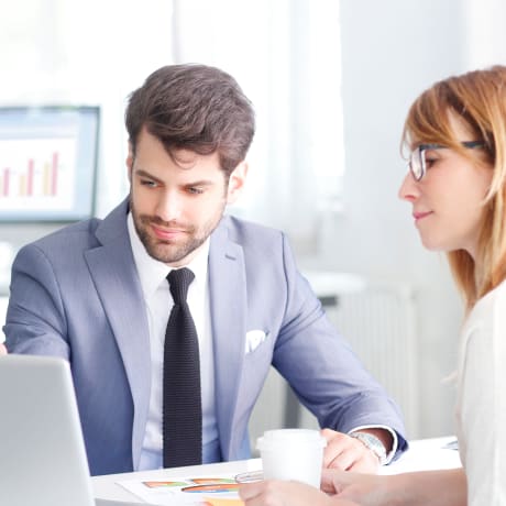 Two people sit in an office looking at a laptop.