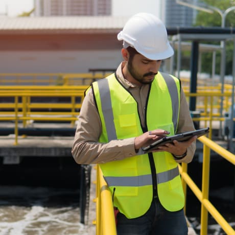 Person in a white hard hat and a hi-viz vest on site using a tablet.